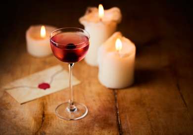Cherry cocktail served on wooden table with three candles.