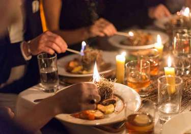 Diners enjoy a meal, lighting herbs on gourmet plates with candles.