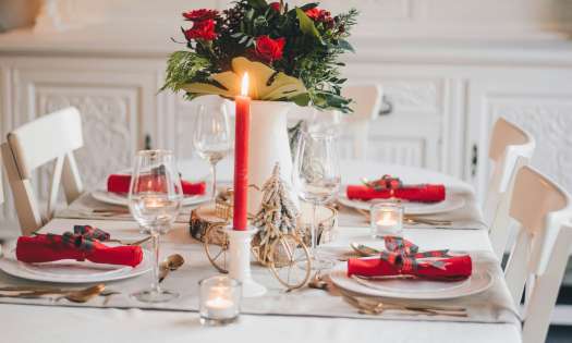 Festive tablespread with red candle and vase of red roses.