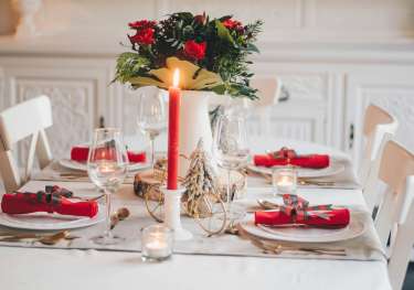 Festive tablespread with red candle and vase of red roses.
