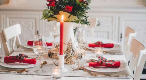 Festive tablespread with red candle and vase of red roses.