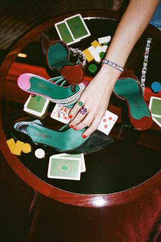 Woman moving shoe on glass table with playing cards.