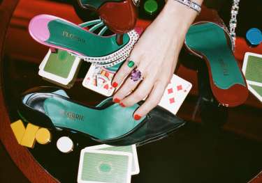 Woman moving shoe on glass table with playing cards.