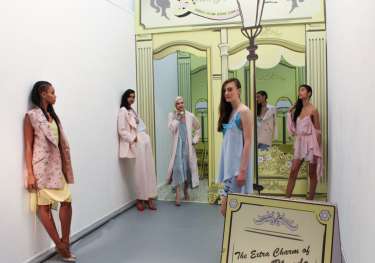 Models stand in a hallway posing amid pastel-colored outfits.