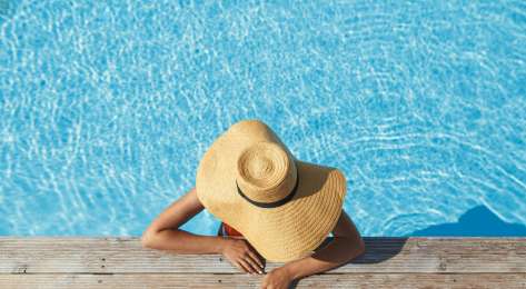 Woman relaxing in pool with wide-brim hat.