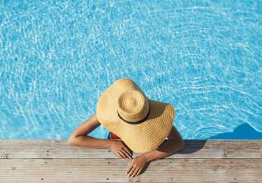 Woman relaxing in pool with wide-brim hat.