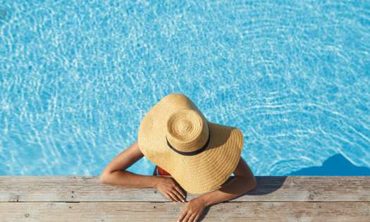 Woman relaxing in pool with wide-brim hat.