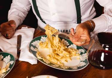 Person tucking into fetuccine alfredo in restaurant.