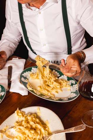 Person tucking into fetuccine alfredo in restaurant.