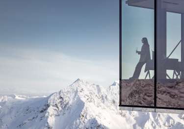 Photo of person drinking wine in restaurant with glass walls looking over snowy mountains.