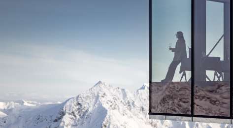 Photo of person drinking wine in restaurant with glass walls looking over snowy mountains.