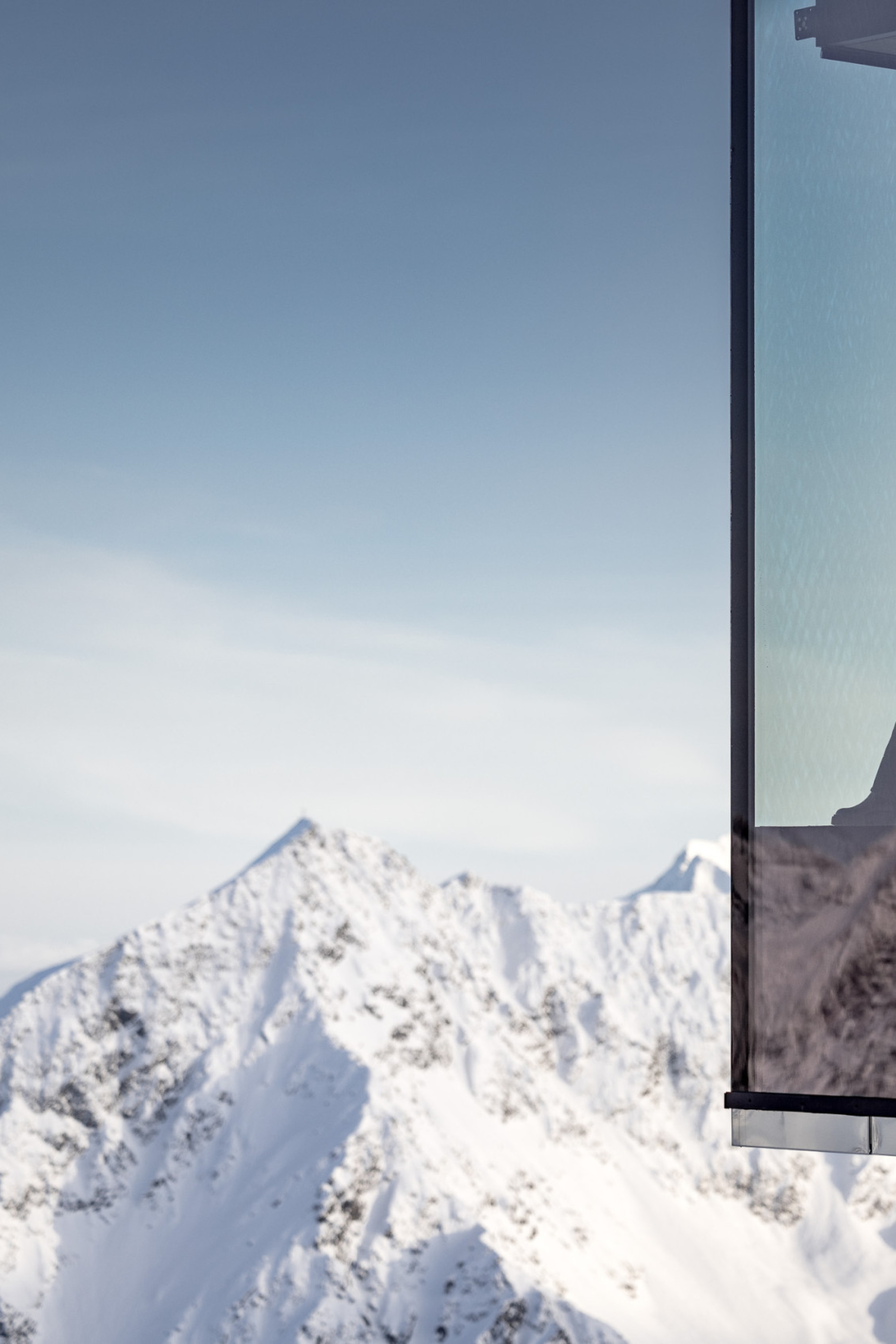photo of person drinking wine in restaurant with glass walls looking over snowy mountains