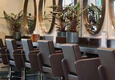 Brown leather chairs and round mirrors inside hair salon.