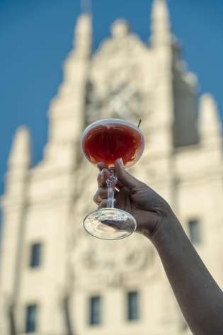 Person holding cocktail against silhouette of building.