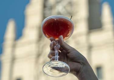 Person holding cocktail against silhouette of building.