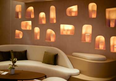 Room inside beauty clinic with curved cream sofa and wall pierced with lights.