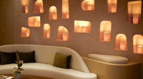 Room inside beauty clinic with curved cream sofa and wall pierced with lights.