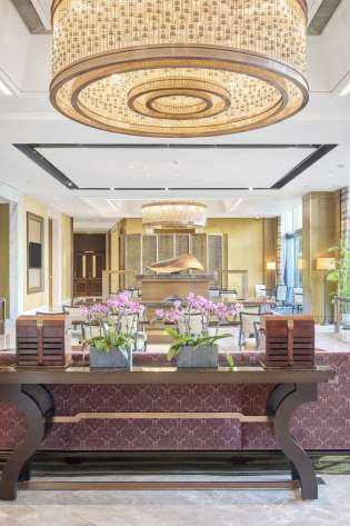 Lobby area in luxurious residential property with grand lighting and burgundy sofas.
