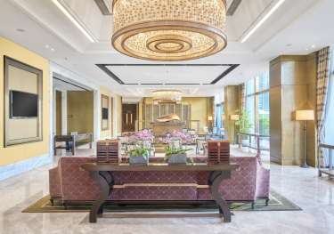 Lobby area in luxurious residential property with grand lighting and burgundy sofas.