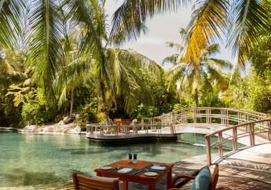 Photo of table and chairs positioned by bridge and pool of water.