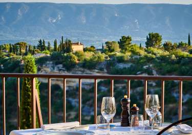 A table set with white tablecloth and glassware overlooks a scenic landscape of lush greenery and mountains under a clear blue sky.