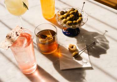 Four cocktails on a marble surface with green olives.