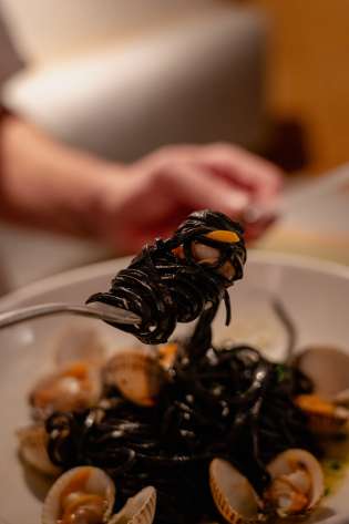 Person twirling black linguine with clams .