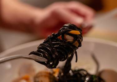 Person twirling black linguine with clams .