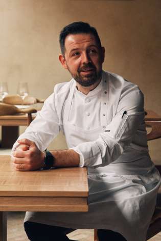 Chef sat in whites at dining table.