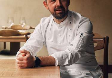 Chef sat in whites at dining table.
