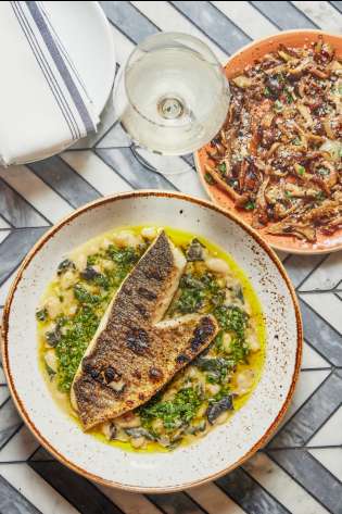 Fish dish served on tiled table with glass of wine.