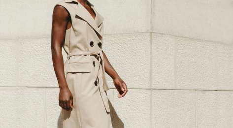 Model wearing sleeveless trench coat in beige.