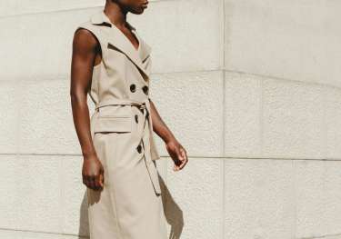Model wearing sleeveless trench coat in beige.