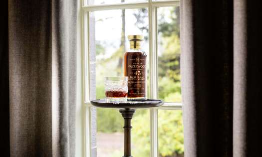 Bottle of whisky and whisky glass styled next to window .