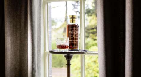 Bottle of whisky and whisky glass styled next to window .