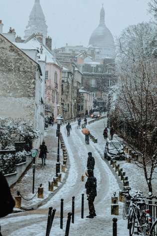 People walking down road in parisian neighbourhood during winter with snow.