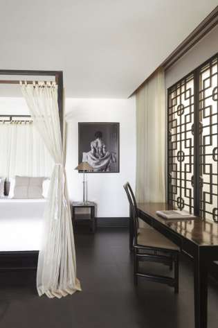 Hotel bedroom in thailand with four-posted bed and wooden desk.