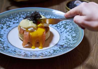 Person cutting into eggs royale topped with caviar.