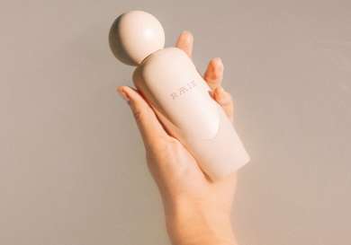 Person holding skincare bottle in pool of milky water.