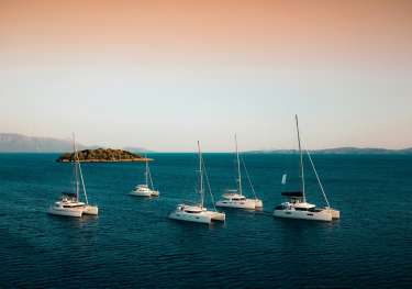 Six luxury yachts in the water with the setting sun behind them.