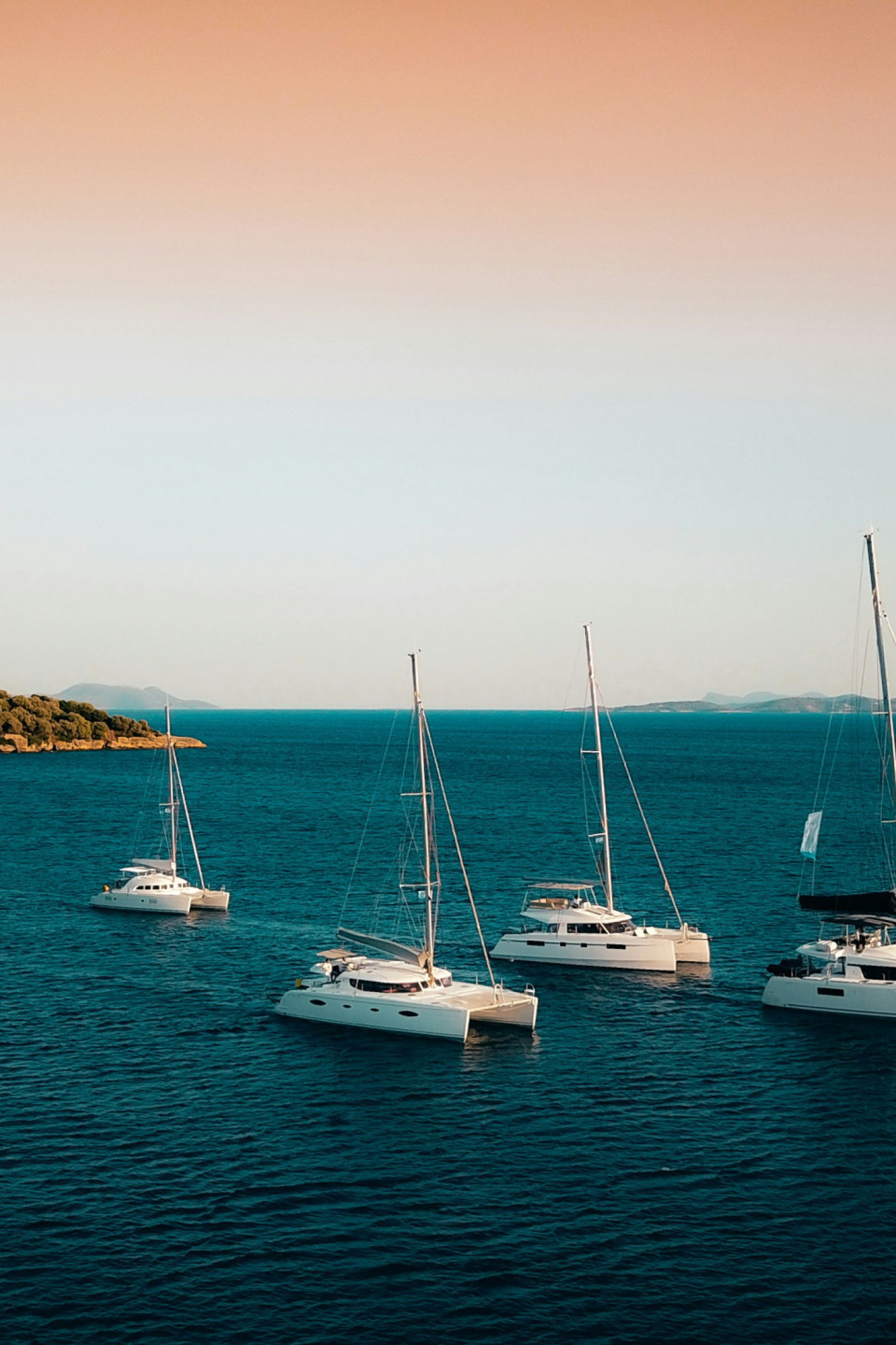 six luxury yachts in the water with the setting sun behind them