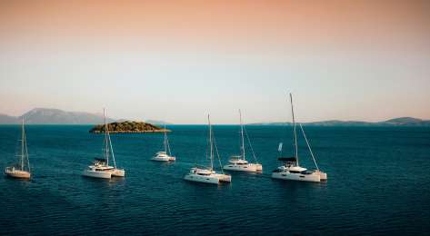 Six luxury yachts in the water with the setting sun behind them.