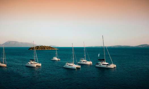 Six luxury yachts in the water with the setting sun behind them.
