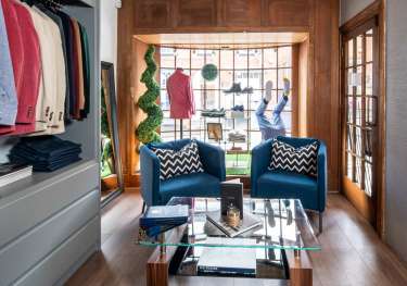 Two blue armchairs face a glass coffee table in a stylish clothing store.