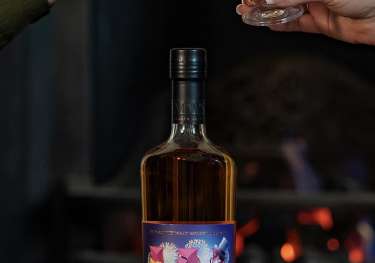 Bottle of whisky and two people clinking glasses.