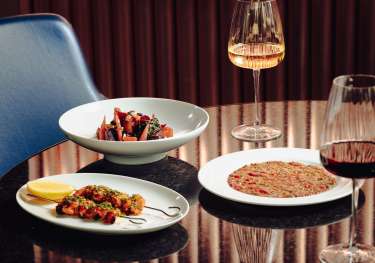 Three dishes and two glasses of wine on restaurant table .