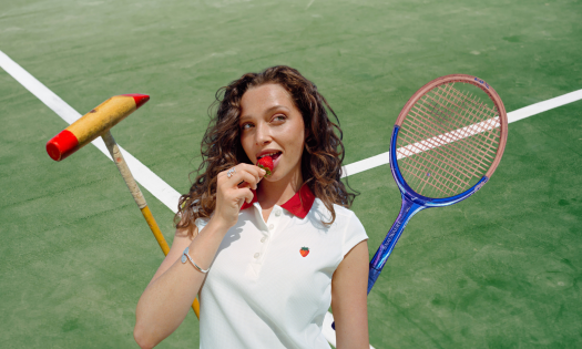 Model posing in wimbledon strawberry-inspired collection with tennis racket and polo mallet.
