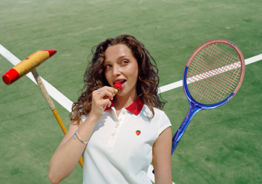 Model posing in wimbledon strawberry-inspired collection with tennis racket and polo mallet.