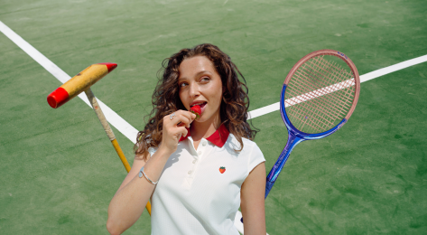 Model posing in wimbledon strawberry-inspired collection with tennis racket and polo mallet.