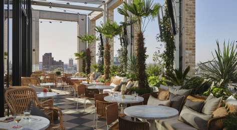 Rooftop bar with round tables, chairs, and plants .